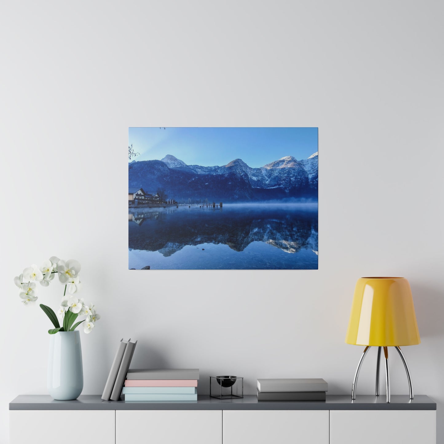 Reflective lake with snowy peaks, a village on the shore, and a clear blue sky. The calm waters create a perfect mirror image of the mountains.