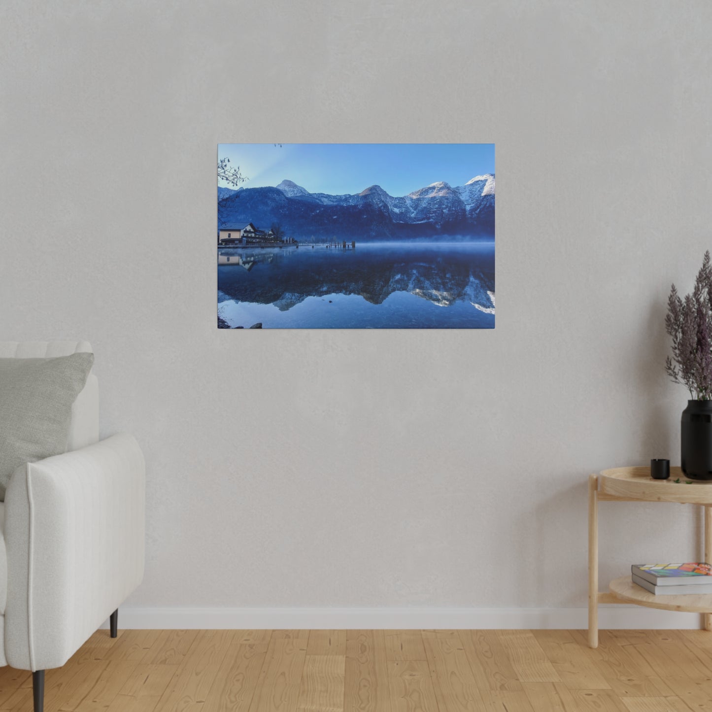 Serene snowy mountains reflected in a lake, with a village on the shore and a bright blue sky. The calm waters create a peaceful and picturesque winter scene.