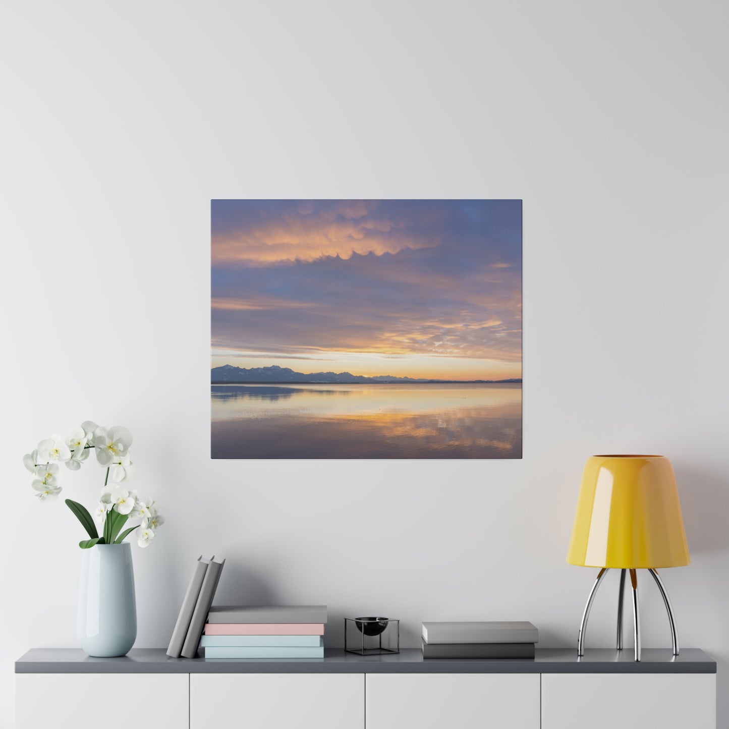A serene sunset over a calm lake, with soft clouds painted in hues of orange and purple. The peaceful scene is reflected beautifully on the still water.