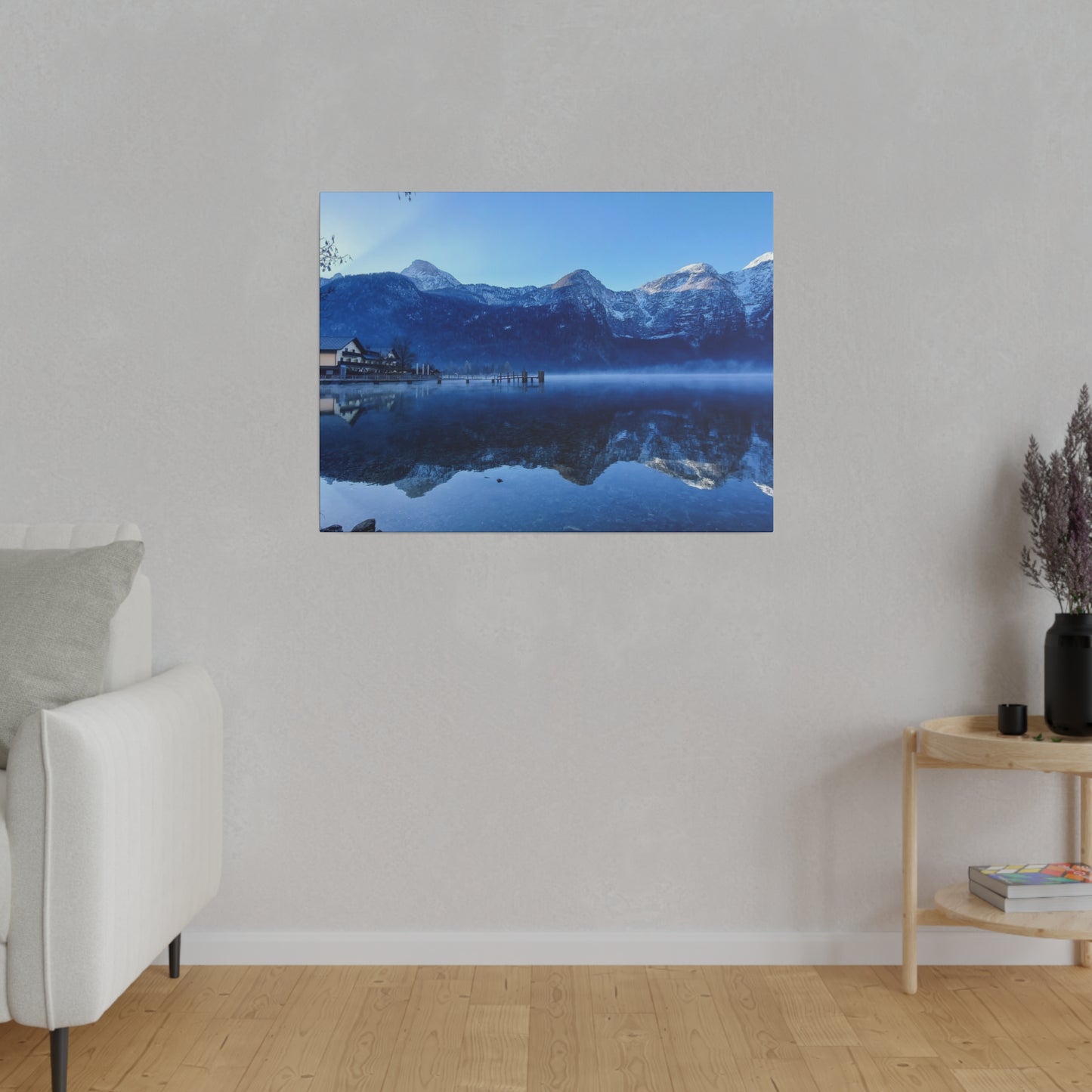 Snowy mountain lake view with calm waters reflecting the peaks and a village on the shore, under a clear blue sky. The scene is peaceful and serene.