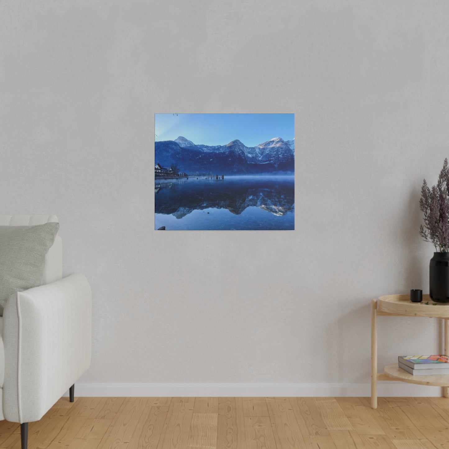 Snowy mountains reflected in a calm lake, with a village and dock on the left, under a clear blue sky. The pristine reflection emphasizes the untouched beauty of the landscape.