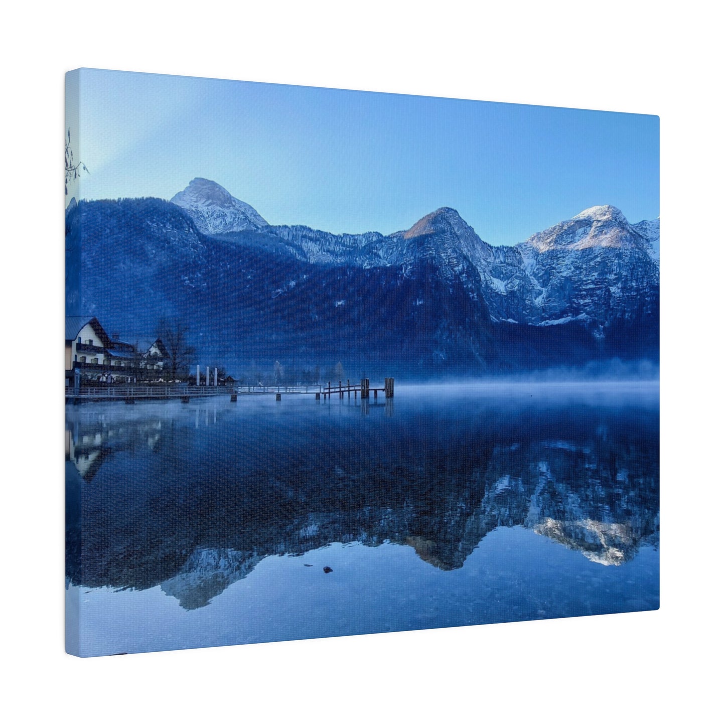 Snowy peaks reflected in a calm lake, with a village on the shore and a clear blue sky. The still waters create a peaceful and serene view.