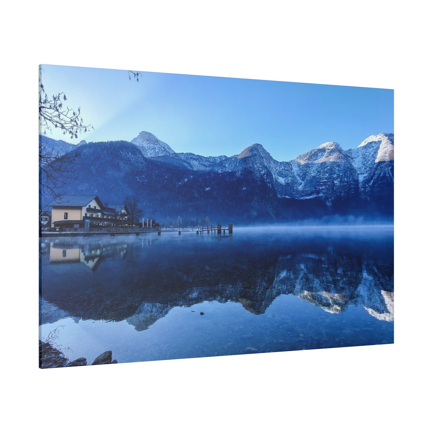 A still mountain reflection with calm lake waters mirroring snowy peaks, a village on the shore, and a bright blue sky. The scene is peaceful and serene.