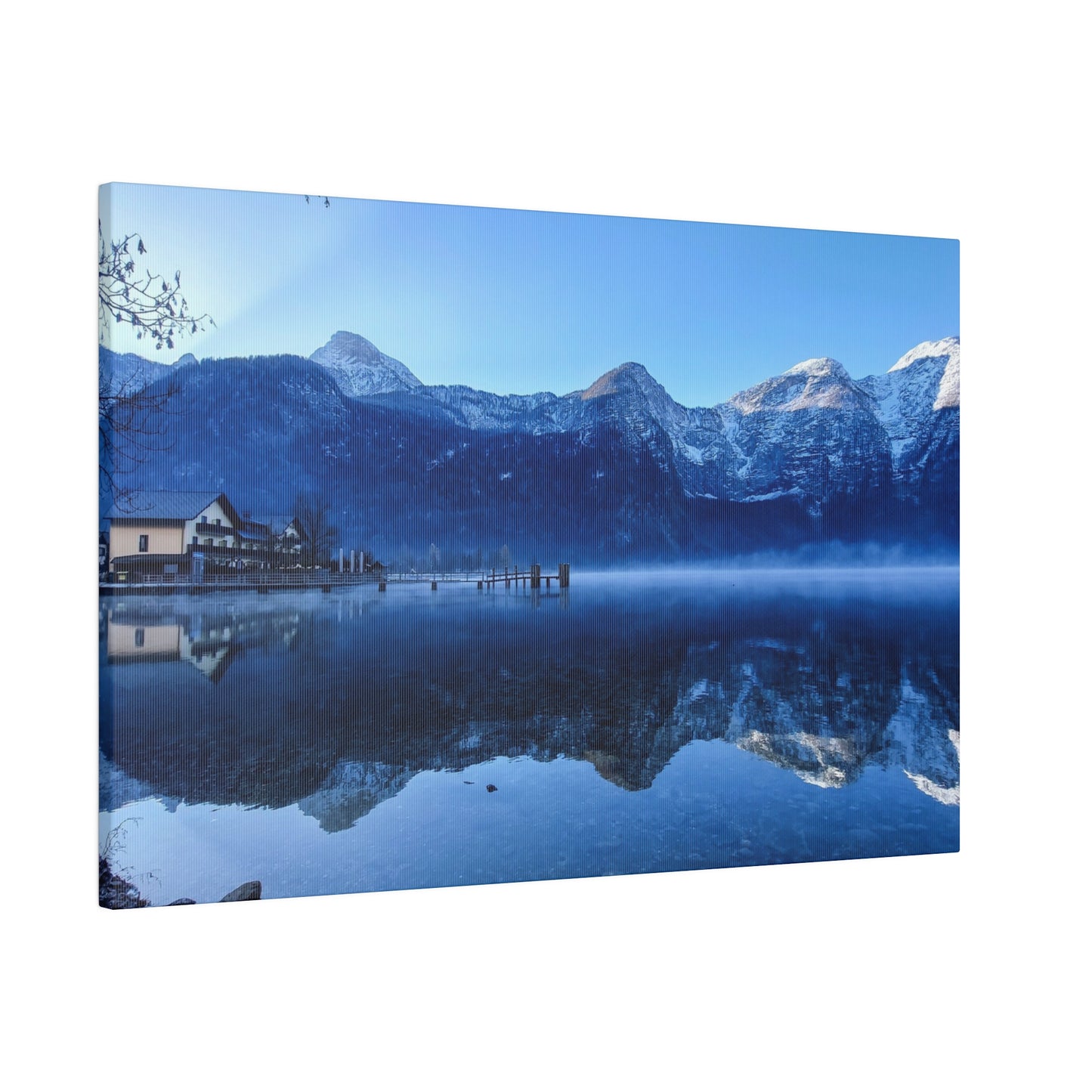 Still waters of a lake reflecting snowy mountains and a village with a dock, under a clear blue sky. The serene reflection creates a sense of calm and tranquility.