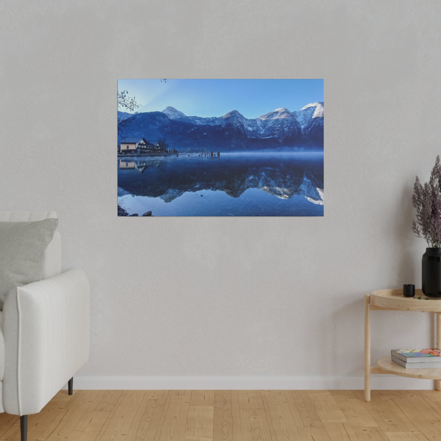 A tranquil lake scene with still waters reflecting snowy mountains, a village on the shore, and a clear blue sky. The perfect reflection creates a serene atmosphere.