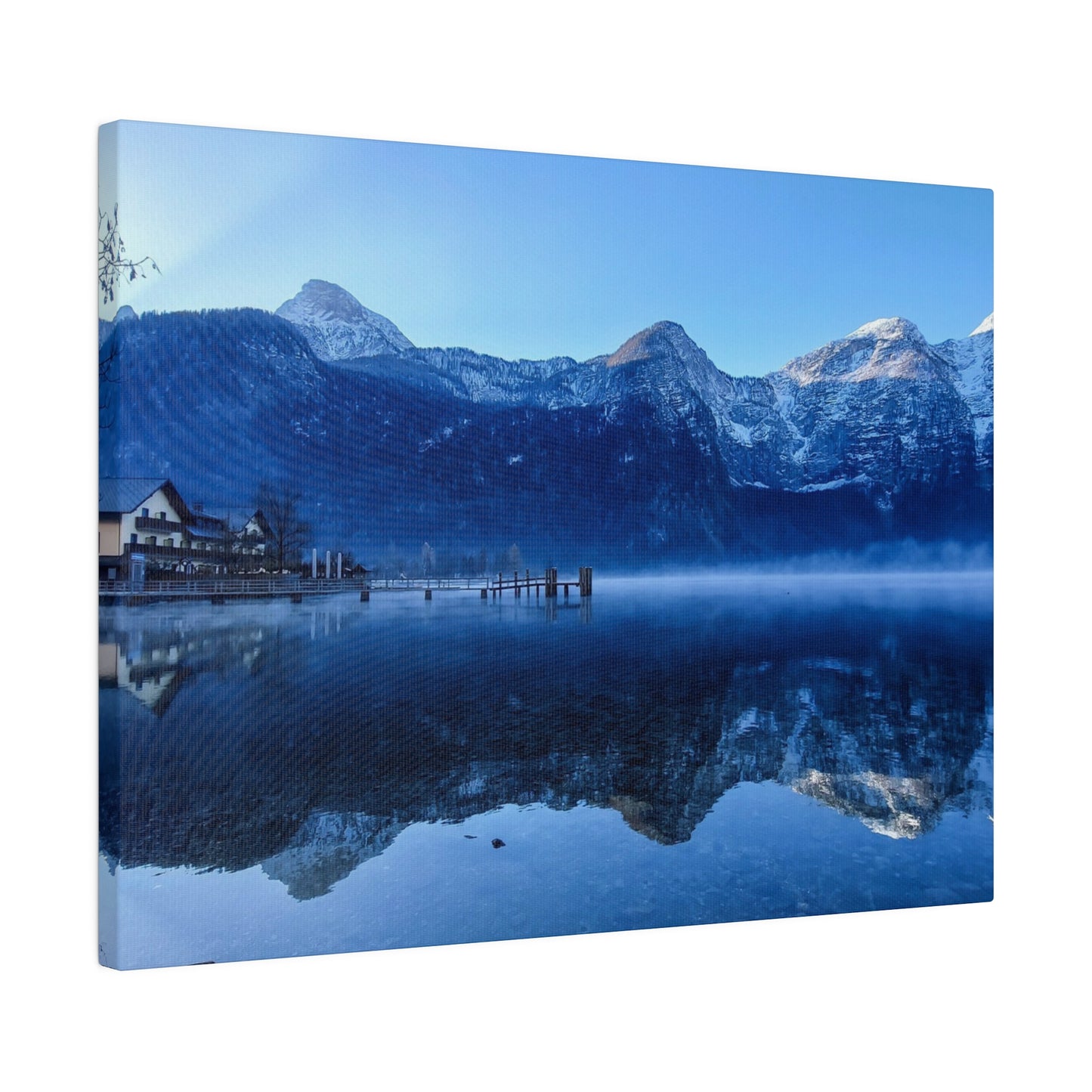 A tranquil lake in winter with still waters reflecting snowy mountains and a village on the shore, under a clear blue sky. The scene is serene and calm.