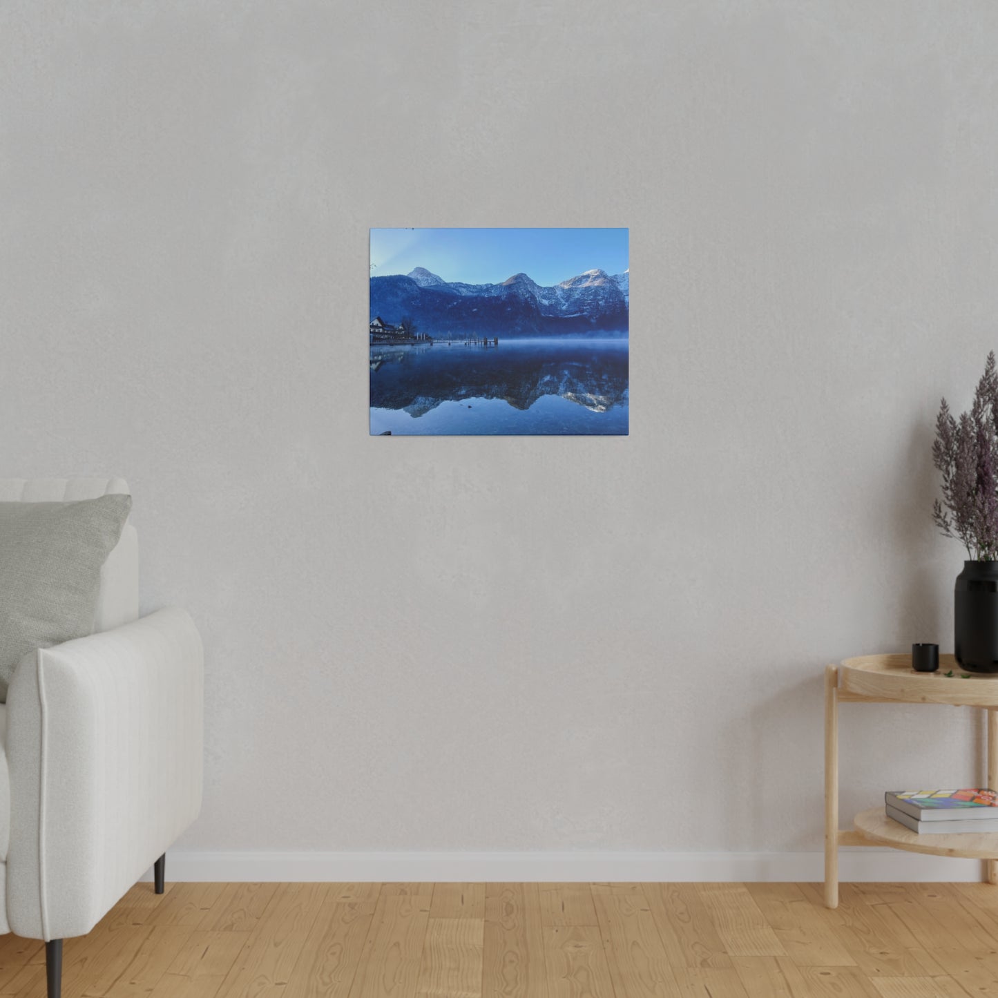 A winter lake with calm waters reflecting snowy mountains and a village on the shore, under a clear blue sky. The scene is peaceful and beautiful.