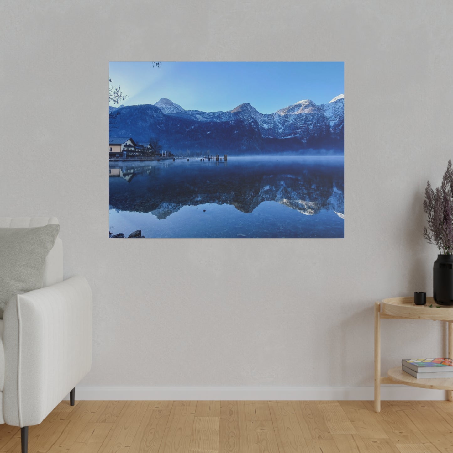 A winter lake reflection with calm waters showing snowy peaks, a village on the shore, and a clear blue sky. The perfect mirror image creates a tranquil atmosphere.