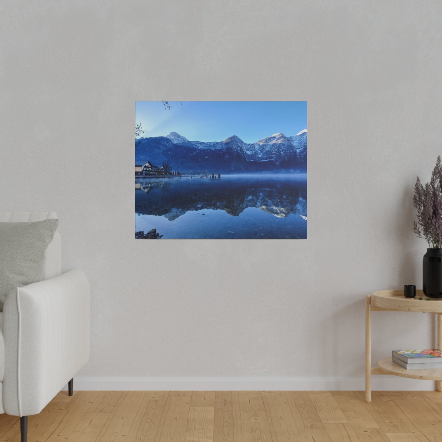 A winter mountain reflection in a calm lake, with a village on the left and a clear blue sky. The snowy peaks are perfectly mirrored in the still waters, creating a serene image.