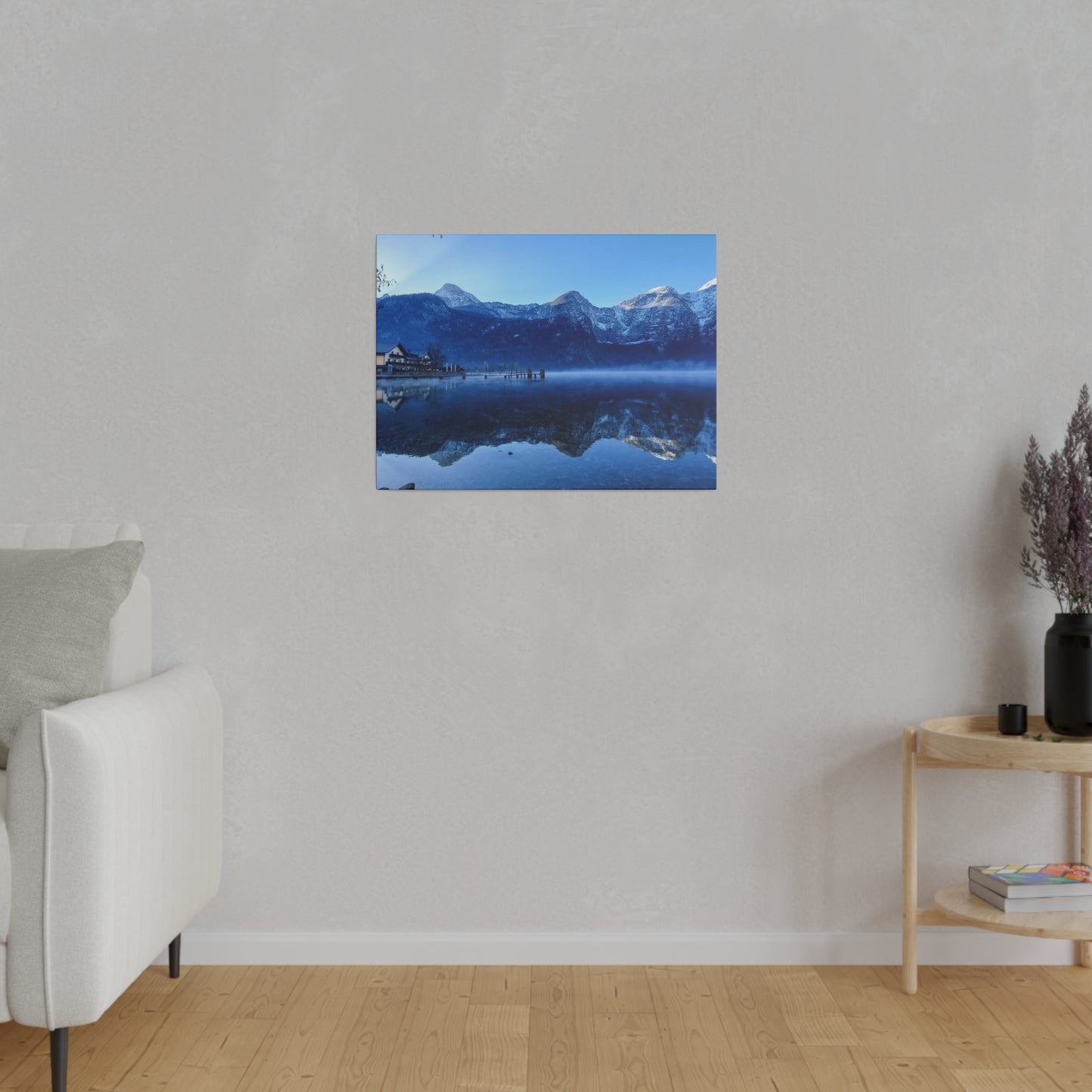 Winter mountain village by a lake, with calm waters reflecting snowy peaks and a bright blue sky. The stillness of the water adds to the serene atmosphere.