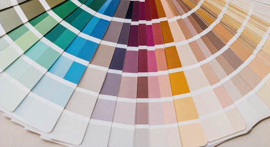 A fanned color swatch deck with rectangular cards arranged in a circular arc, showing a gradient from green to beige.