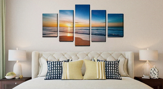 Bedroom with a multi-panel canvas wall art featuring a serene beach sunset above a beige tufted headboard, flanked by modern bedside tables with lamps.