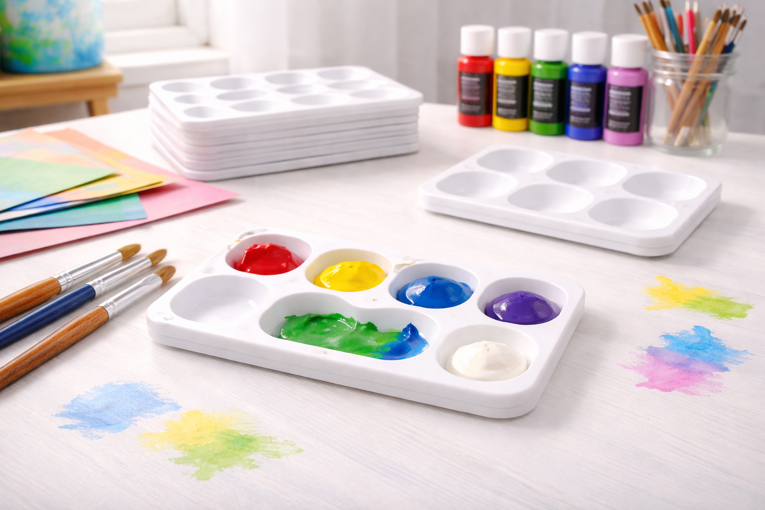 White rectangular 6-well paint tray palettes with colourful paint and brushes arranged on a bright art table in a landscape blog header image.