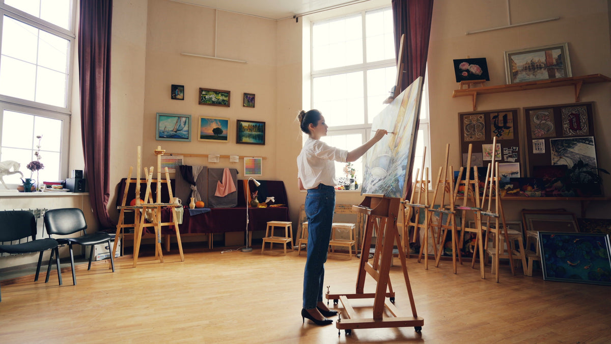 An artist painting on canvas in a bright studio with natural light.