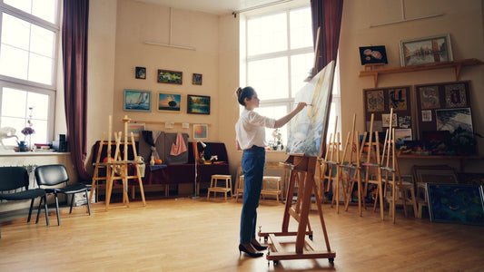 An artist painting on canvas in a bright studio with natural light.