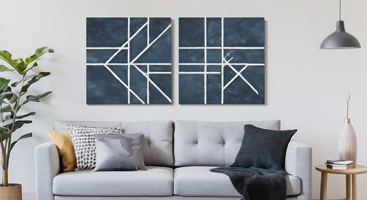 Two navy blue abstract canvases with white geometric lines mounted above a light gray sofa in a bright living room