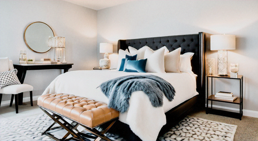 Elegant bedroom with a tufted black headboard, luxurious bedding, and decorative pillows. The room features a stylish bench at the foot of the bed, bedside tables with modern lamps, and a chic vanity with a round mirror.