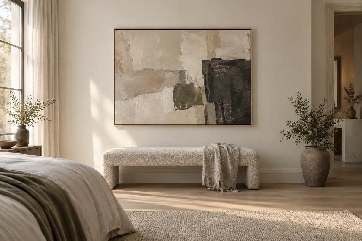 Muted abstract canvas above a light upholstered bedroom bench in a softly lit neutral bedroom