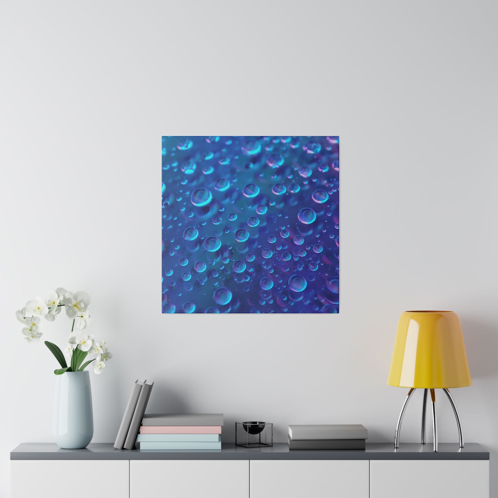 Square blue abstract wall art featuring numerous blue and purple bubbles hanging above a console table with a pale vase.
