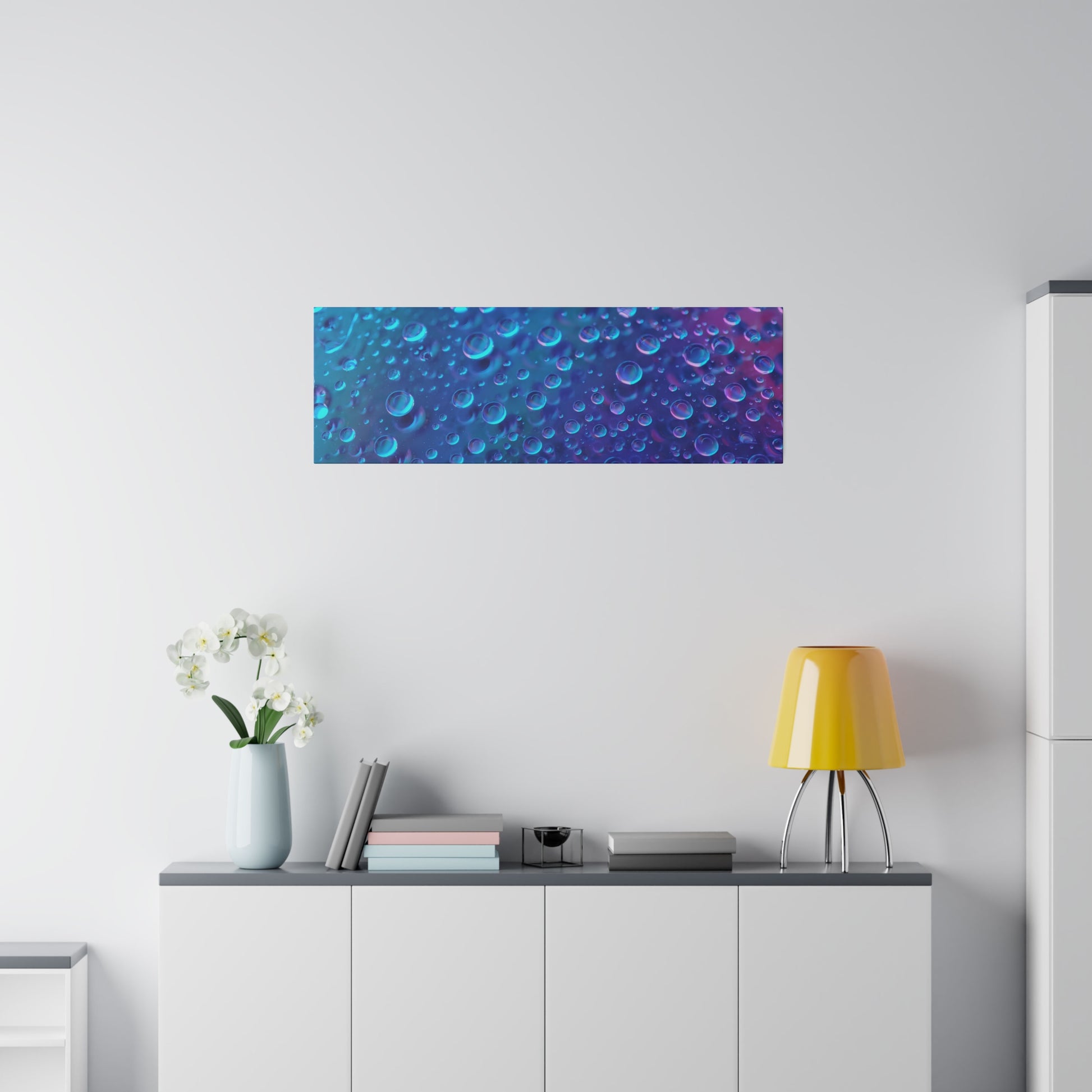 Rectangular wall art with a blue-to-purple bubble pattern mounted above a white cabinet in a minimalist living space.