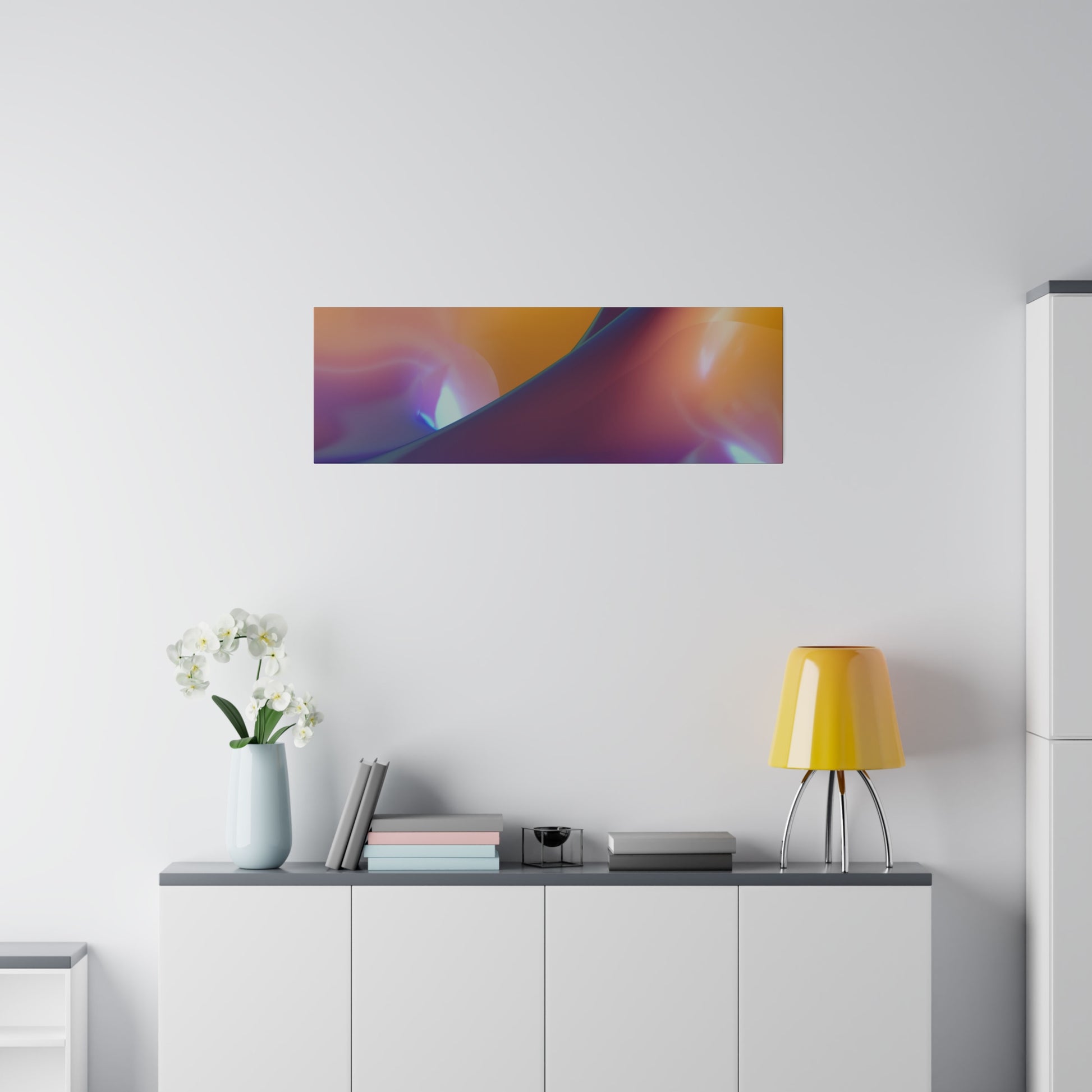 Rectangular abstract wall art with orange, purple and blue gradients mounted above a white cabinet with a yellow desk lamp and a vase of