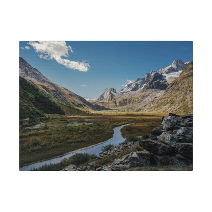 A rocky alpine valley with a winding stream, green meadows, and snow‑capped peaks under a blue sky.