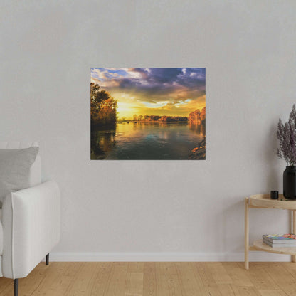 Square landscape painting of a sunset over a calm river with tree-lined banks, mounted on a light gray wall.