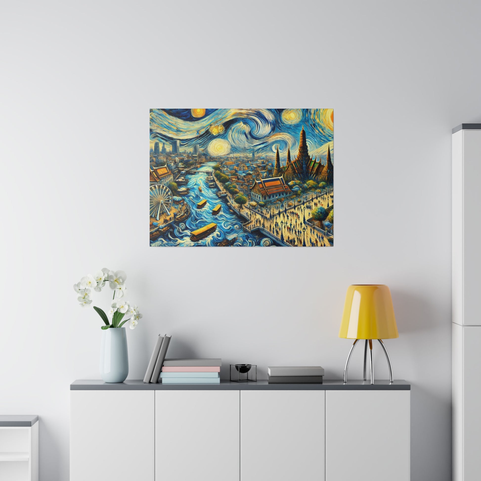 Colorful cityscape painting hung on a white wall above a white cabinet with a yellow lamp and vase of white flowers.