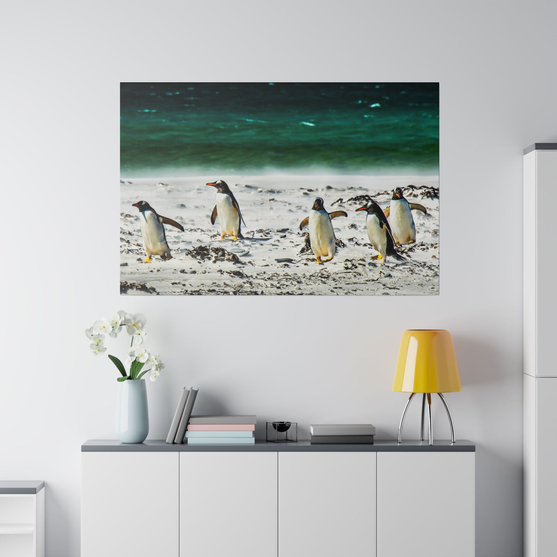 Beach-walking penguins near the ocean, with the vibrant colors of the sea in the background. The scene is tranquil and natural, with sand and seaweed.