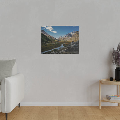 Framed landscape photo of an alpine valley with a winding river, rocky foreground, and snow-capped mountains.
