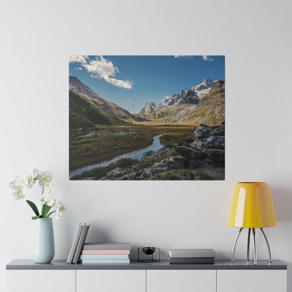 Square landscape photo of a valley with a winding river, rocky foreground, and snow-capped mountains under a blue sky.