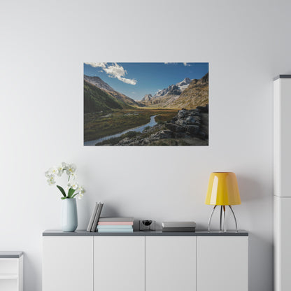 Framed landscape of a mountain valley with a winding river, rocky foreground, and snow-capped peaks under a blue sky.