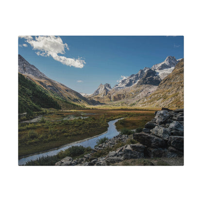 Snow-capped mountains overlook a winding river through a valley with grassy banks and a rocky foreground.