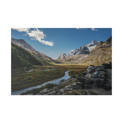 A wide valley with a winding river, surrounded by snow‑capped mountains and rocky slopes under a blue sky.