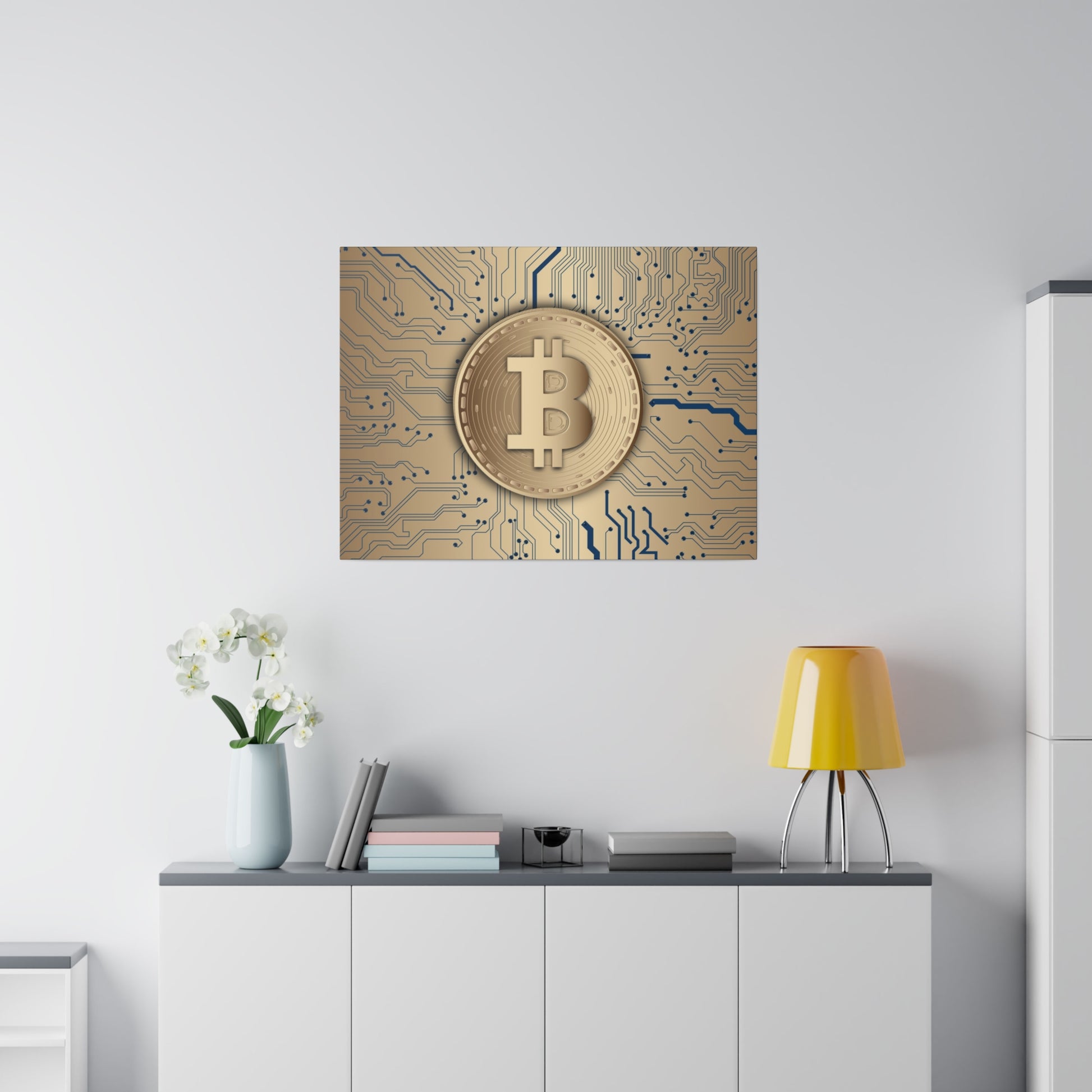 Framed wall art showing a gold Bitcoin coin on a blue circuitry background above a white cabinet with a yellow lamp and a vase.