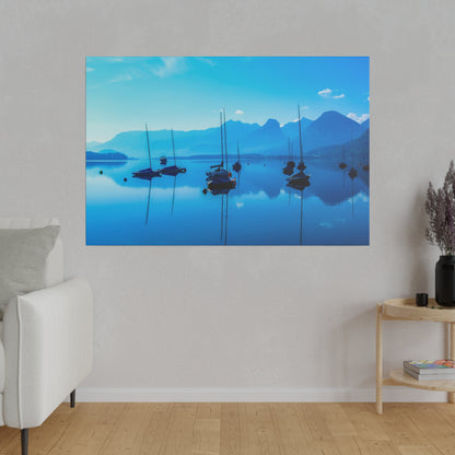 Blue lake scene with several sailboats anchored on calm water, reflections, and blue mountains in the distance.