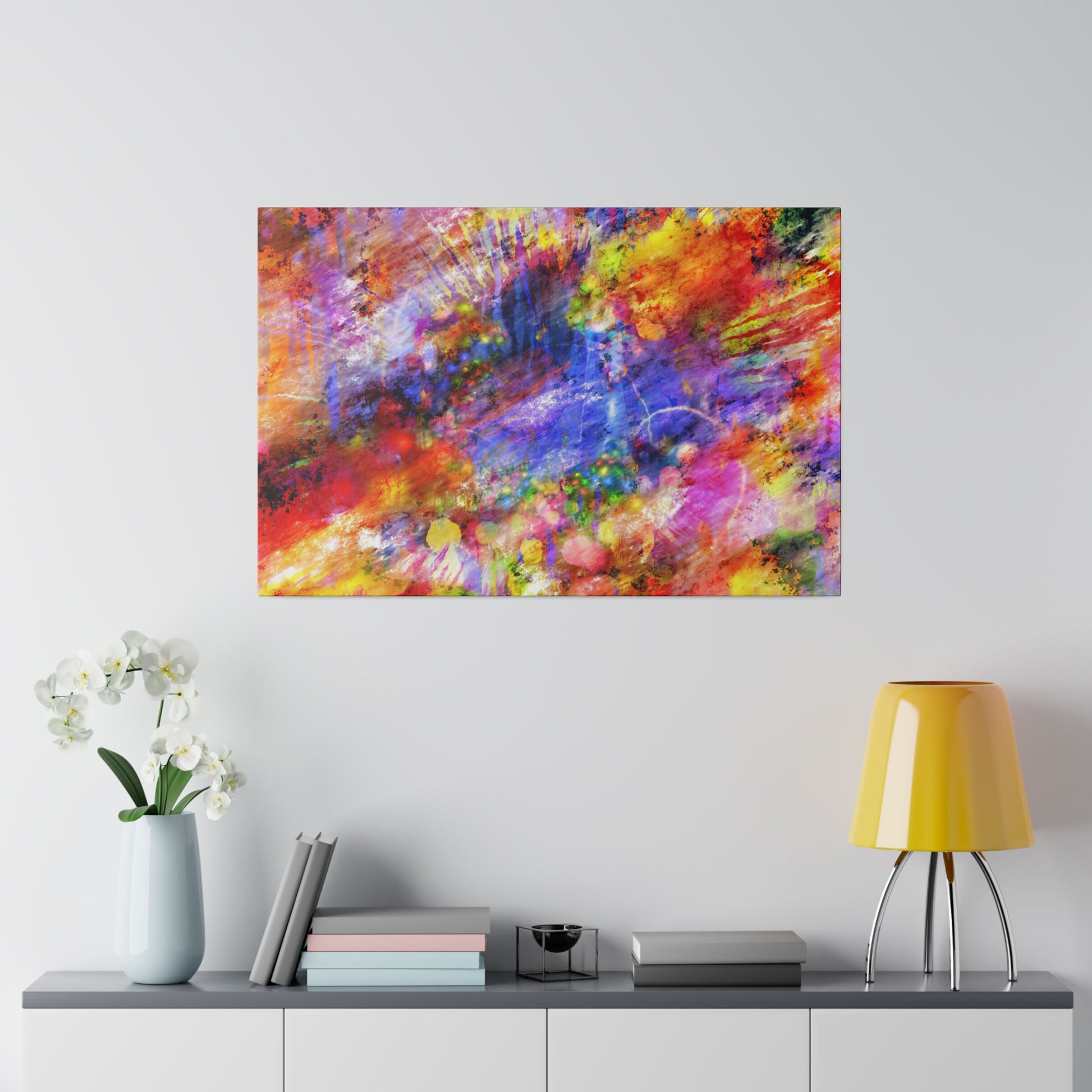 Abstract colorful painting with red, yellow, blue splashes hangs on a light wall above a console with a pale blue vase of white orchids,