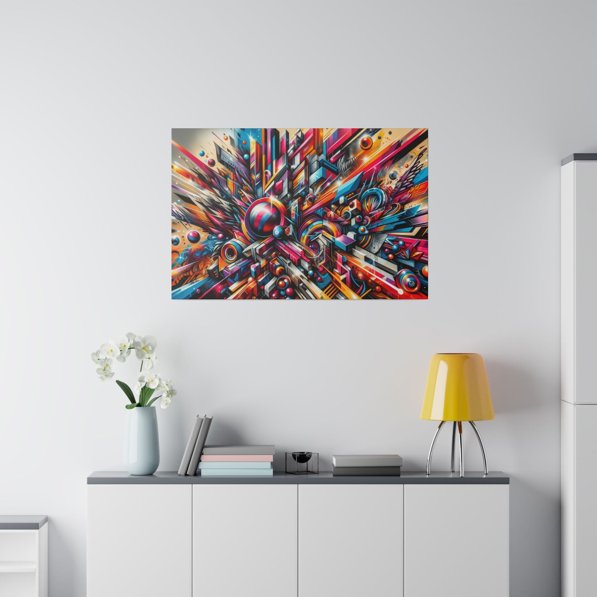 Colorful abstract explosion painting mounted above a white sideboard with a vase of white orchids and a yellow lamp.
