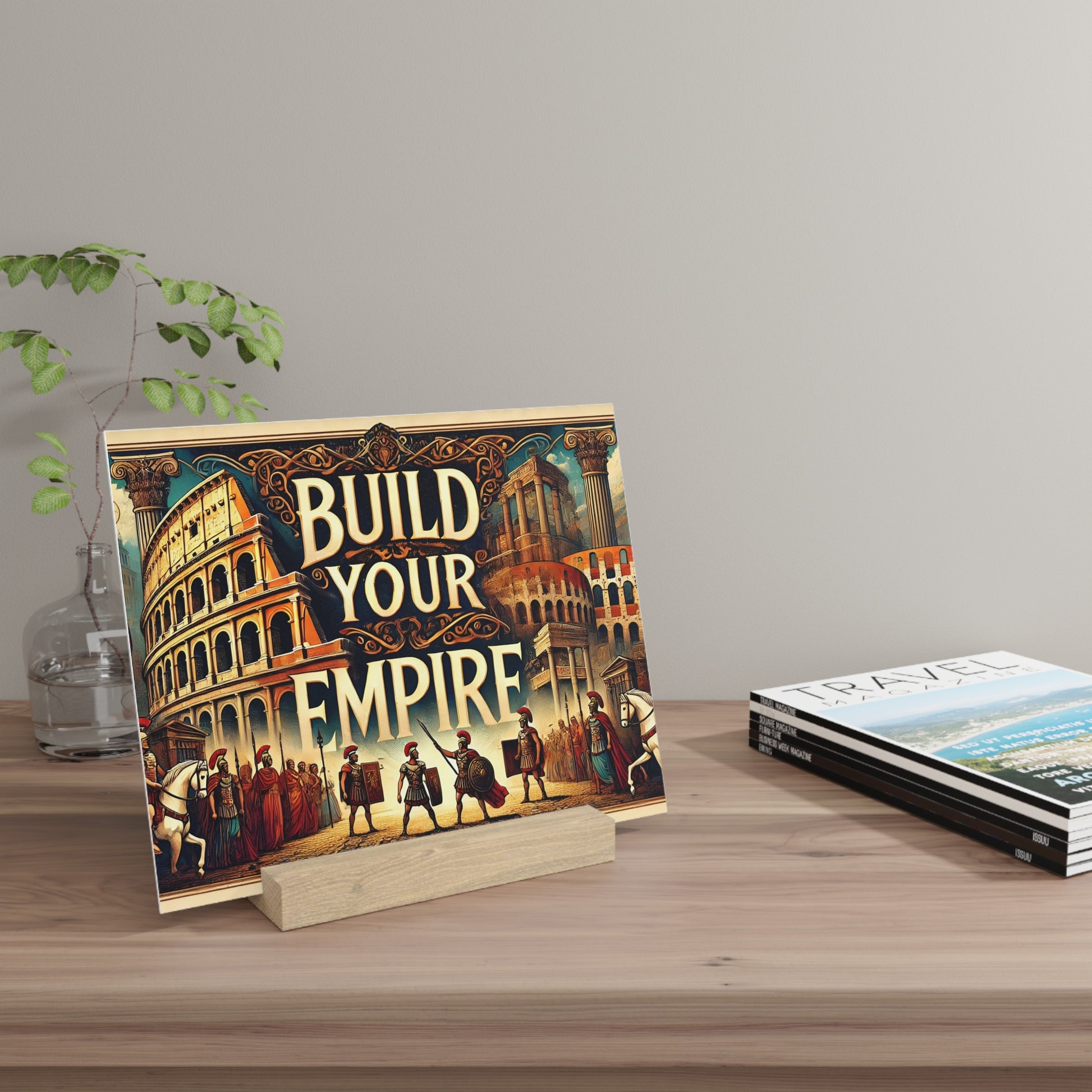Colorful illustrated poster reading "BUILD YOUR EMPIRE" on a wooden stand beside a glass vase with greenery.