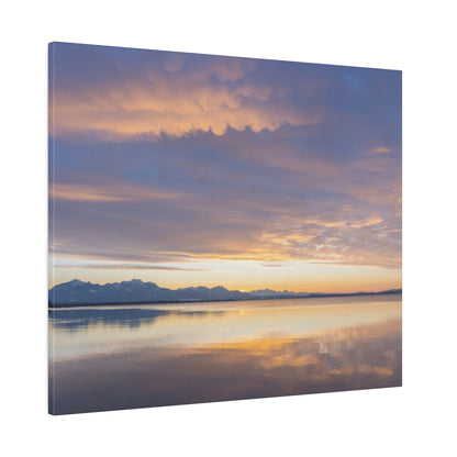 Calm lake at sunset with an orange-blue sky, distant mountain range, and reflections on the water.