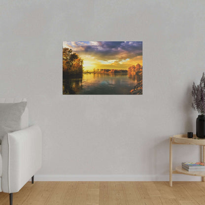 Framed landscape painting of a river at sunset with golden trees along the banks, hung on a light gray wall.
