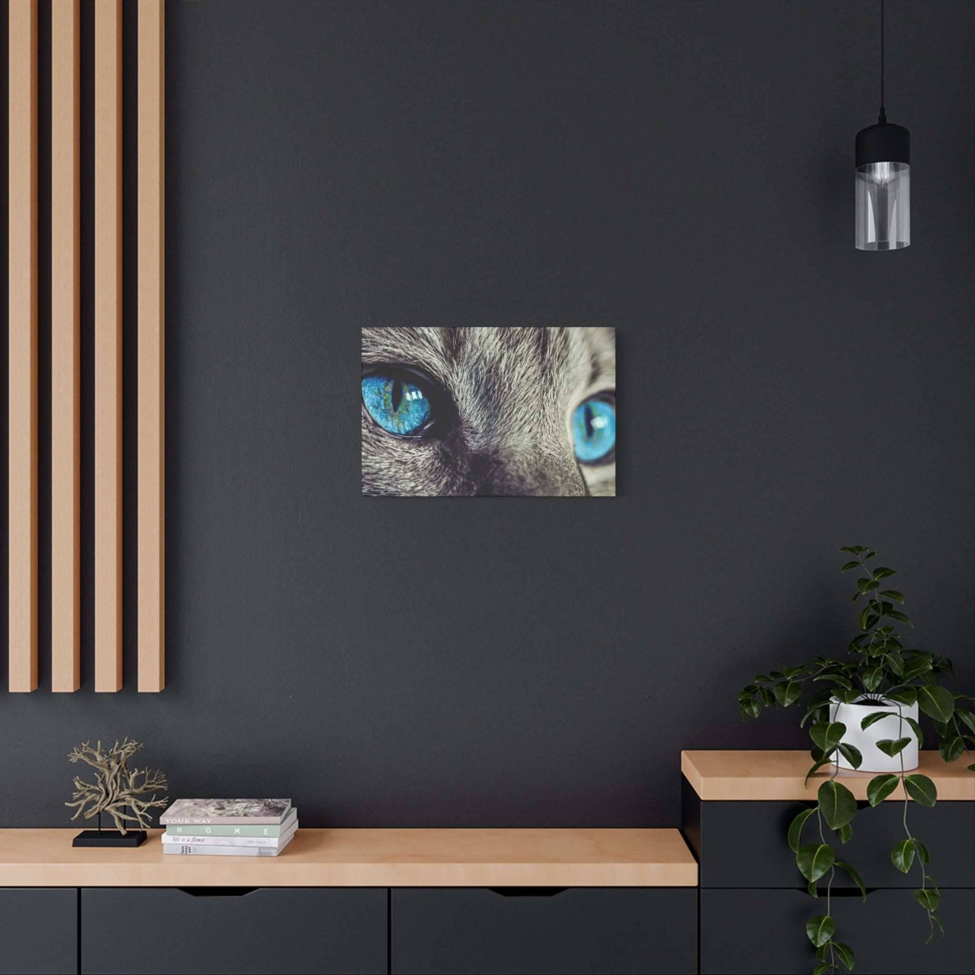 Close-up of a cat's blue eyes on a small square canvas hung on a dark wall.