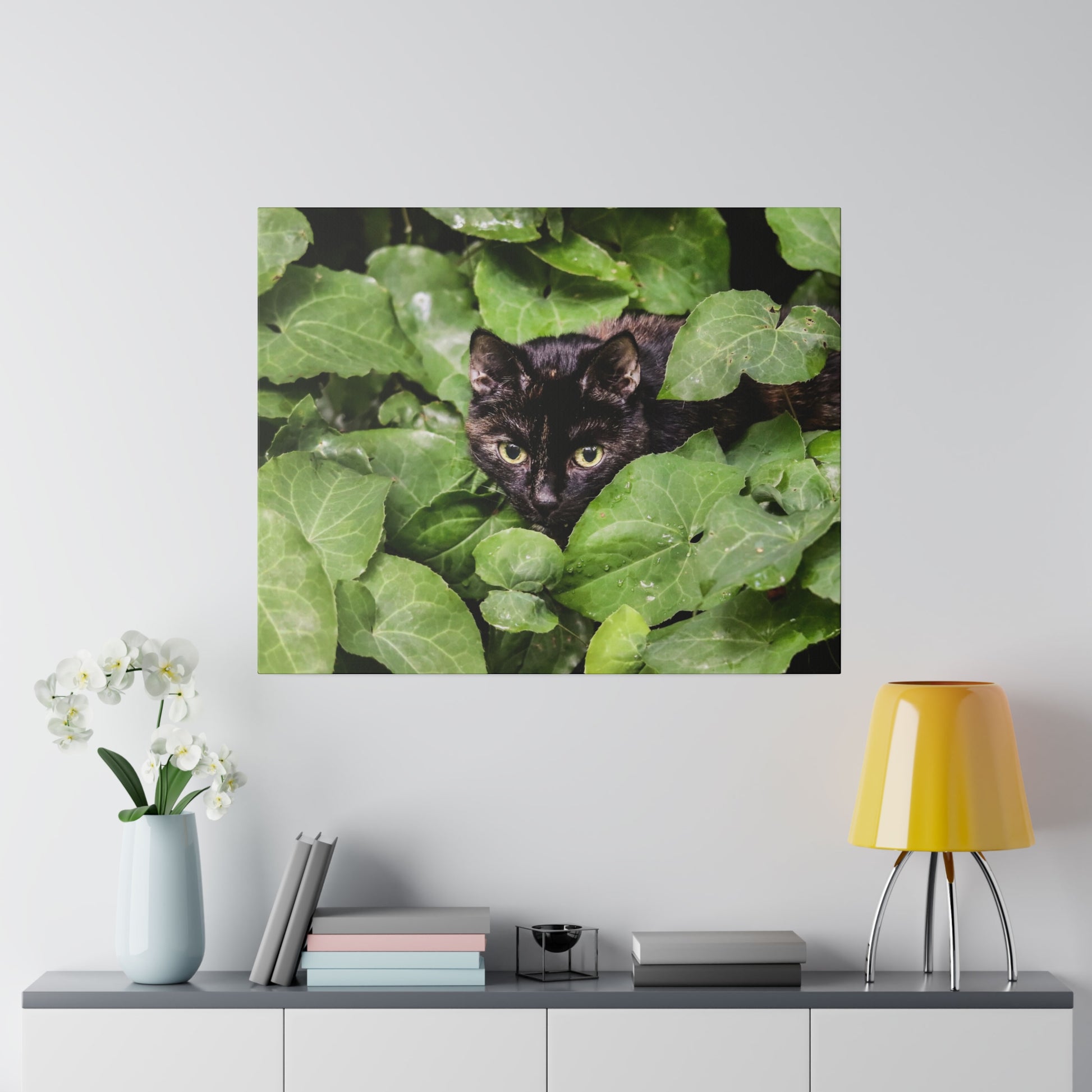 Close-up of a black cat peering through dense green ivy leaves.