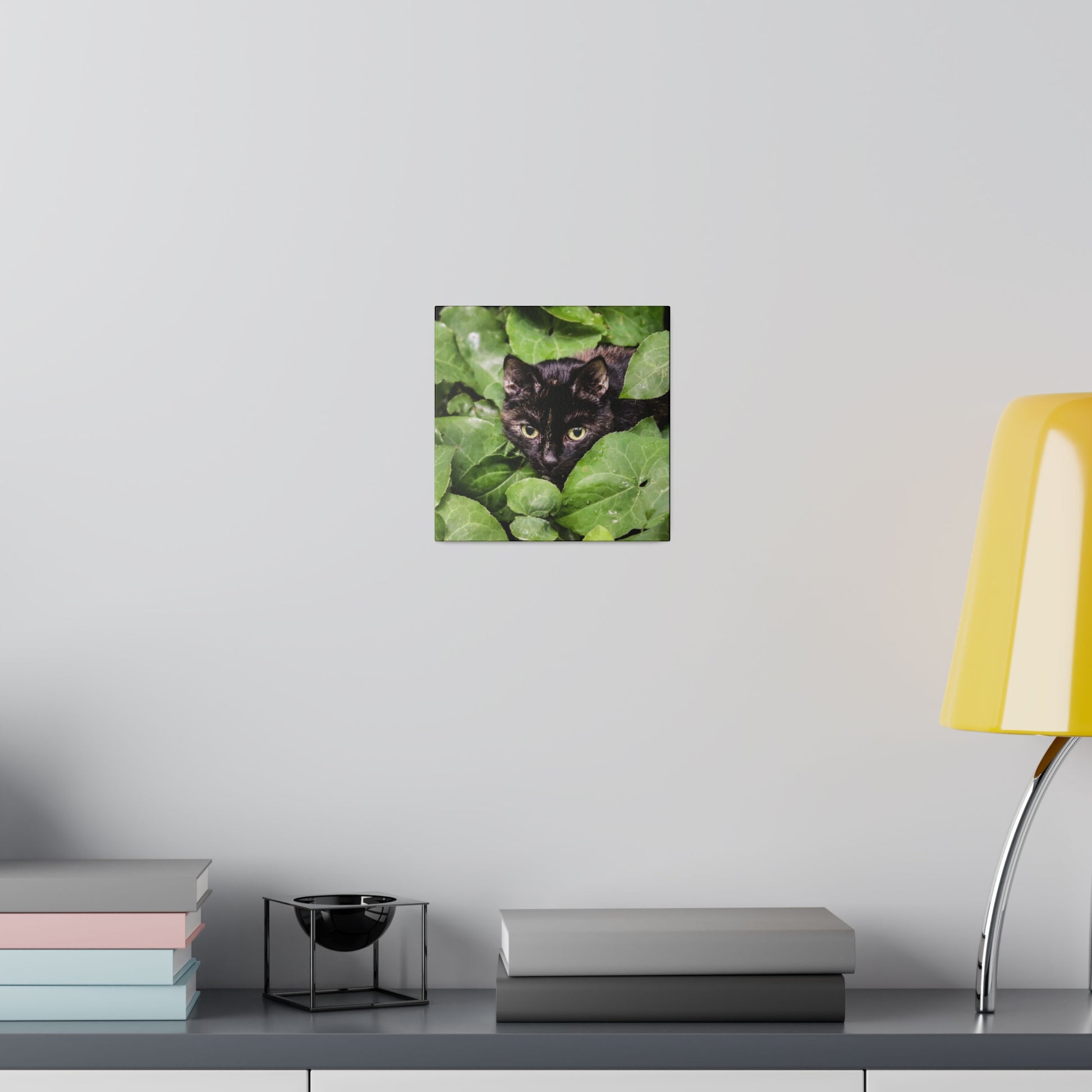 Small square wall art showing a black cat's face peeking through green ivy leaves.