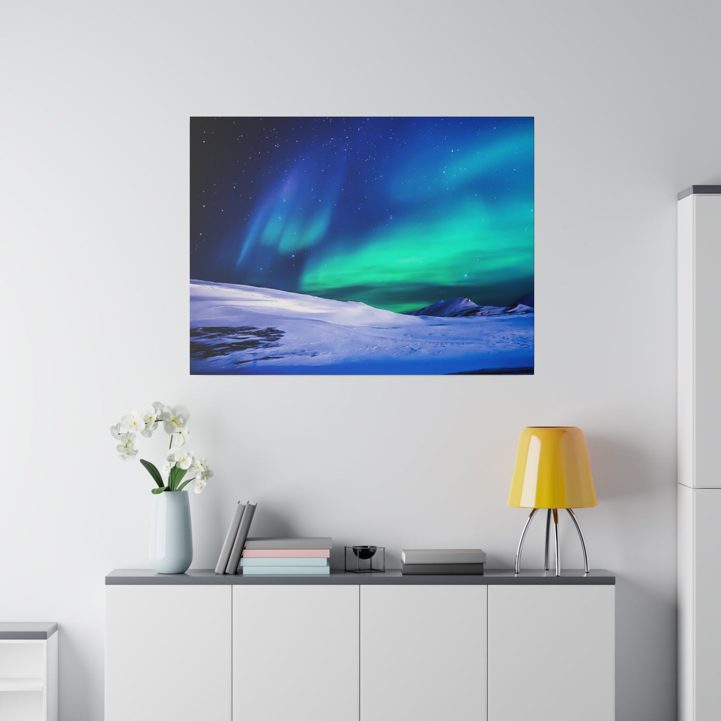 Square wall art depicting the northern lights over a snowy landscape hung above a white cabinet.