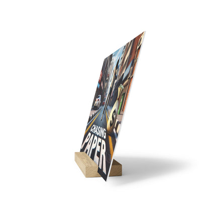 Poster on a wooden display stand angled upright, showing a city street illustration and the title "CHASING PAPER".