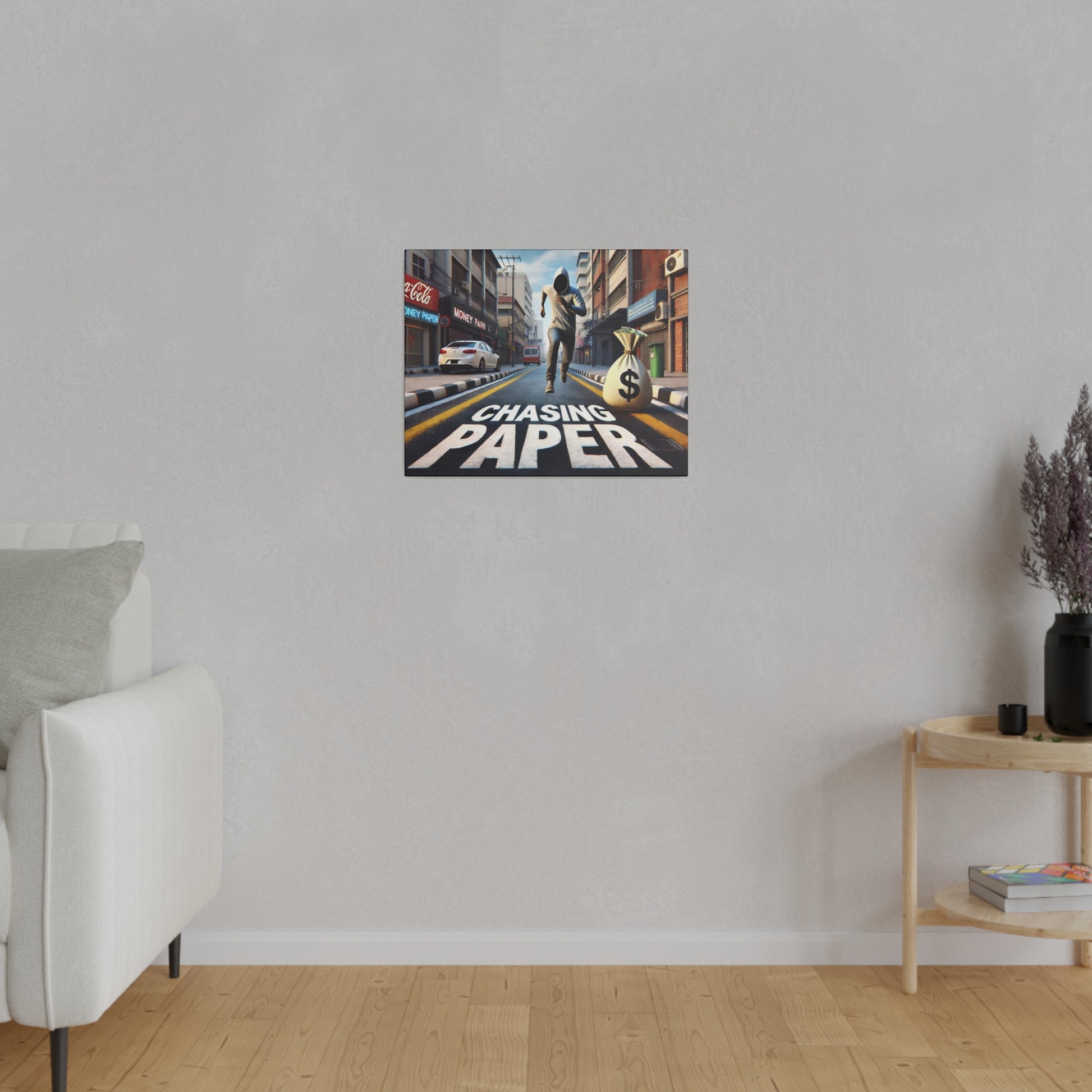 Small framed poster on a light gray wall shows a city street with a money bag and the text “Chasing Paper.”