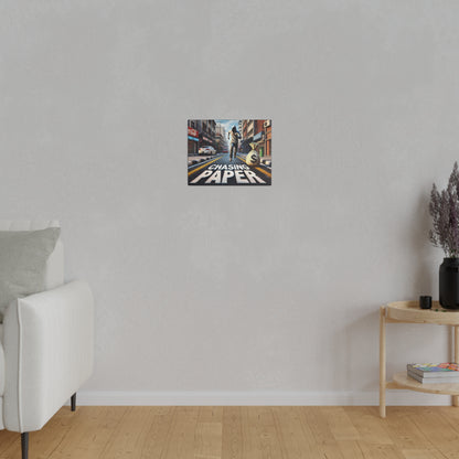Small rectangular poster on a light gray wall showing a city street scene with a person walking and the text “Chasing Paper” in bold white