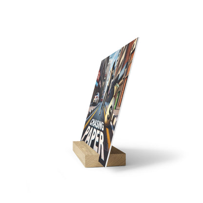 A printed poster showing a city street scene with the text 'Chasing Paper,' angled on a light wooden block stand.