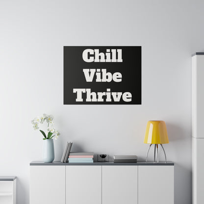 Black wall art with bold white text “Chill Vibe Thrive” hangs above a white cabinet in a minimal living room with a yellow lamp and vase.